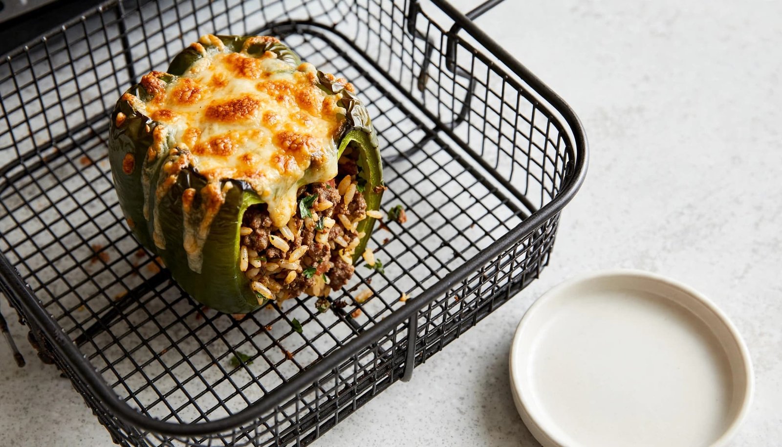 A stuffed bell pepper with melted cheese reheats in an open air fryer basket.