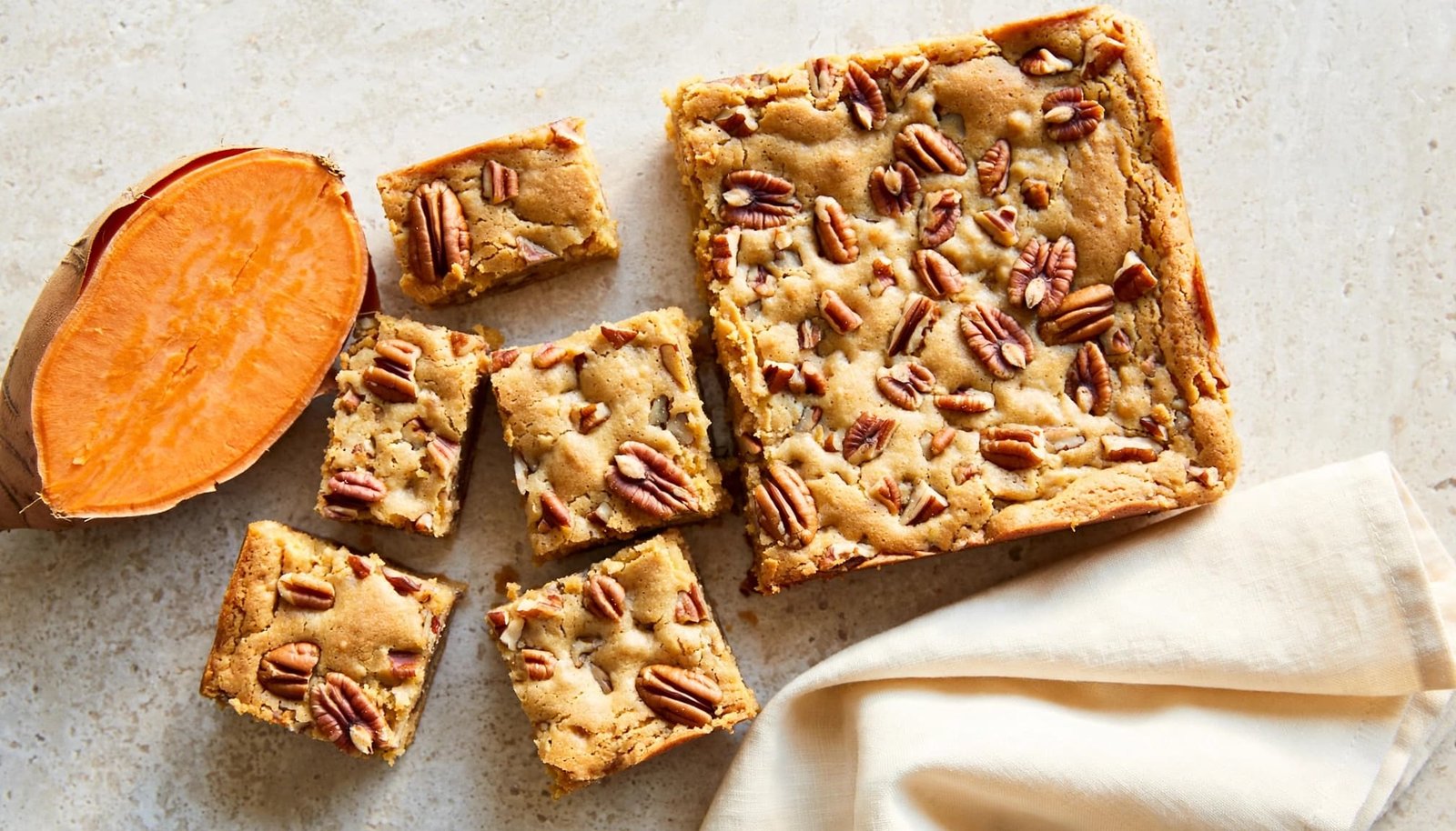 Sweet potato blondie squares with pecans beside a halved sweet potato and cream napkin.